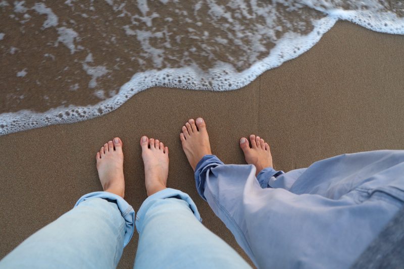 Friends standing barefoot near the water on a sandy beach.